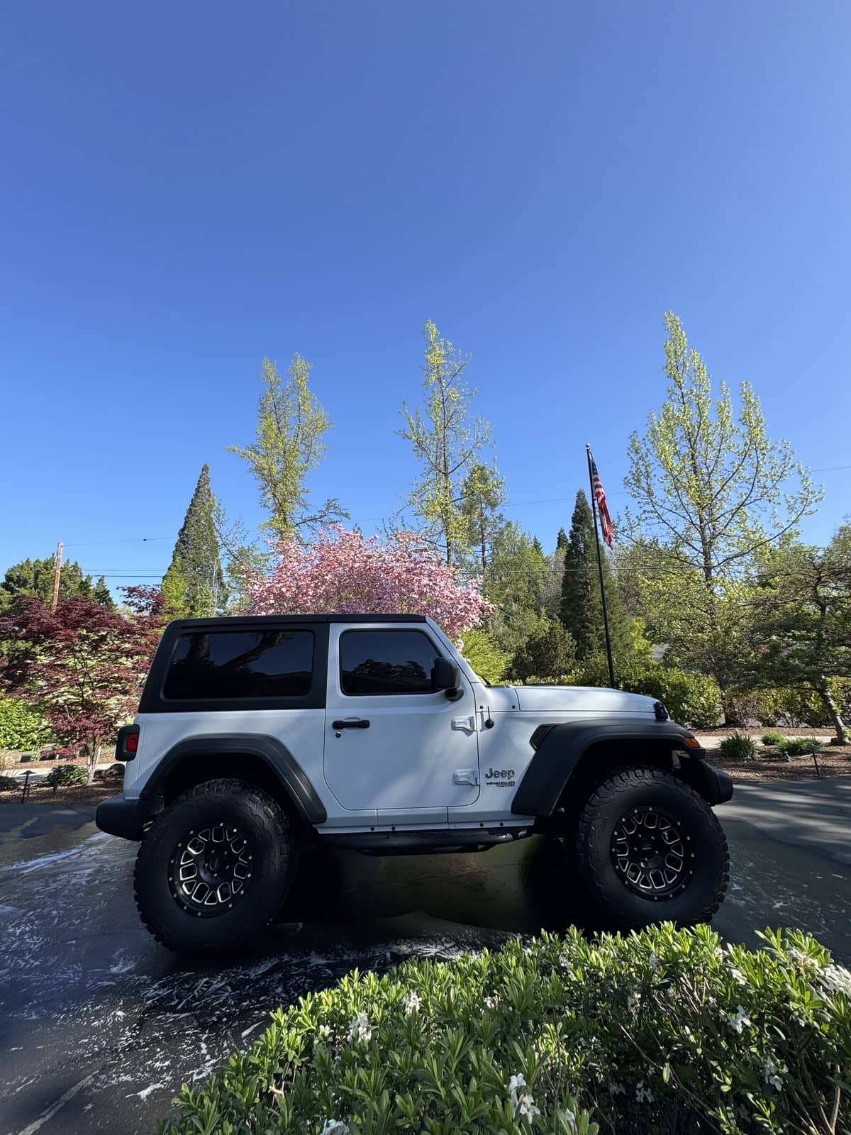 White Jeep parked on a wet driveway surrounded by garden landscaping.
